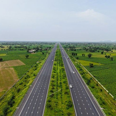 Aerial view of a wide, multi-lane national highway cutting through lush green fields. Discover prime highway plots, industrial land, and commercial setups for sale in Hapur with our premier Real Estate Services in Delhi NCR.