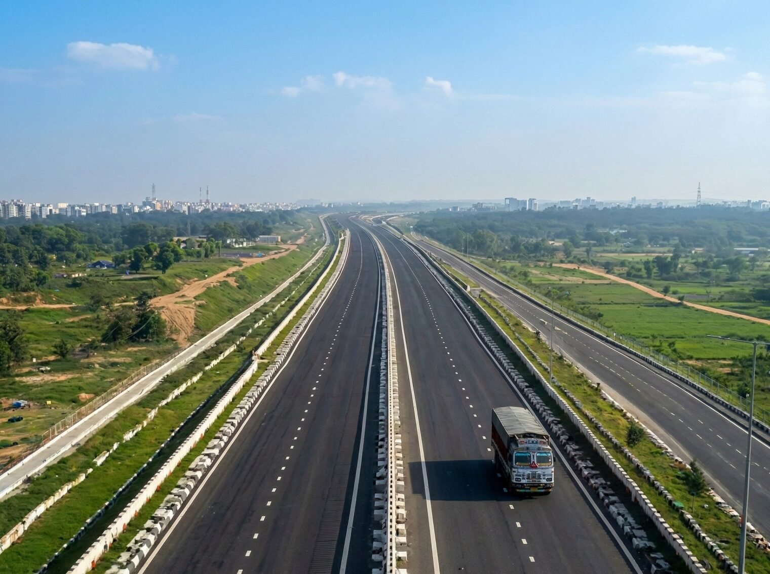 Aerial view of a wide multi-lane highway surrounded by green landscapes. Explore high ROI highway land acquisitions on NH334 and NH9 with the most Trusted Property Dealer in Delhi NCR.