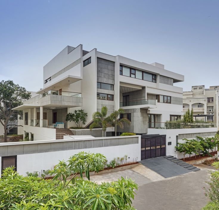 Exterior view of a modern, multi-story luxury villa with a paved driveway. We provide top-tier Real Estate Services in Delhi NCR, helping buyers find beautiful independent houses and luxury villas for sale in Noida, Ghaziabad, and Hapur.