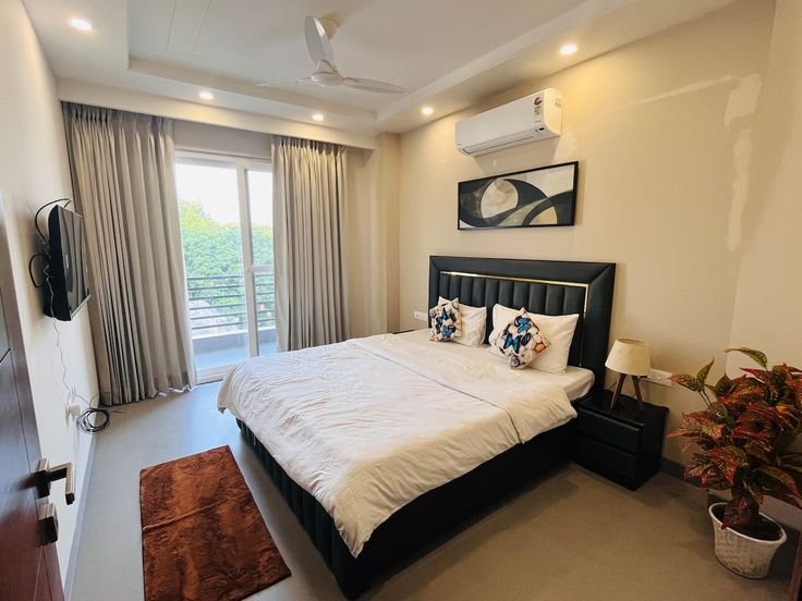 A beautifully furnished modern bedroom in a rental apartment with balcony access. Explore affordable rental houses, stylish studio apartments, and prime Airbnb properties in Noida and Ghaziabad with the best Real Estate Services in Delhi NCR.